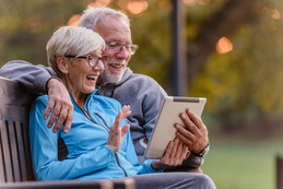 Two people with white hair sitting outside looking at a tablet.