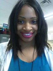 Erika, a Black woman with shoulder length straight hair, smiles into the camera. She's wearing pink lipstick, a blue tshirt, and a white cardigan. 