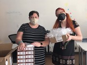 two health care workers holding boxes of COVID-19 tests for the disability community