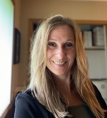 A headshot of Sarah, a middle-aged white woman  with long blonde hair in an office interior.