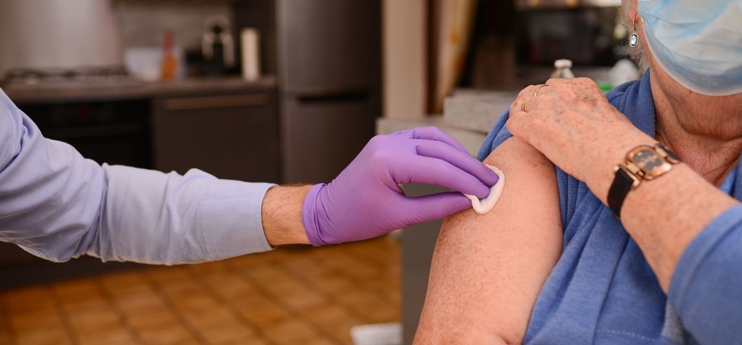 provider disinfecting arm of patient receiving vaccine with gloved hand