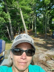 Selfie of Kaia, a woman with pale skin and shoulder-length silver hair. She's wearing a grey baseball cap with wolves on it and sunglasses.