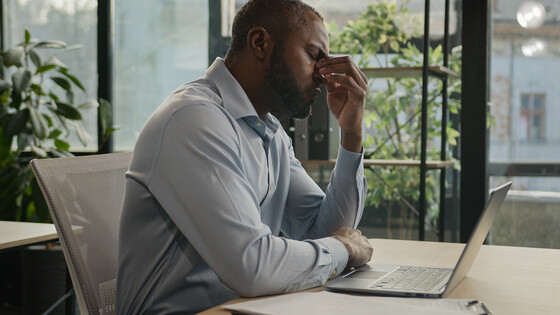 Tired man, at computer, holds his head in his hand