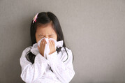 child sneezing into facial tissue