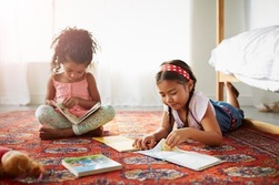 Two children sitting on the floor reading 