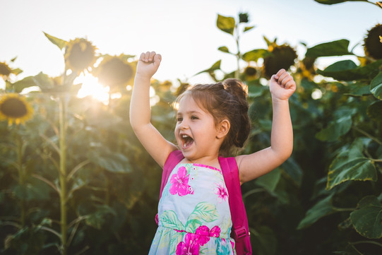 child outside arms raised in front of sunflowers