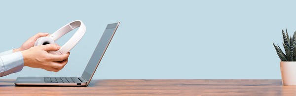 A pair of hands holding headphones near a computer with a potted plant on desk