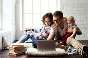 two adults with infant sitting on floor with computer