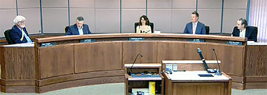 Five council members seated on curved dais in Council Chambers, spaced apart, faces can be seen without masks. 