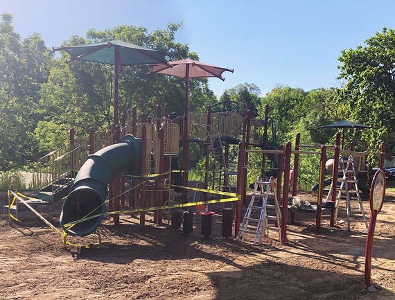 Playground structure with tunnel slide, three overhead canopies, steps and elevated platforms wrapped in yellow tape.