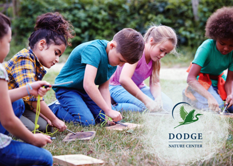 Five children kneeling on grass looking down and rubbing tool over wooden block. Dodge Nature Center logo.