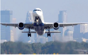 Airplane with nose facing forward lifting off from runway, city buildings in background.
