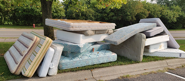 pile of old mattresses and box springs stacked near curbside at the park