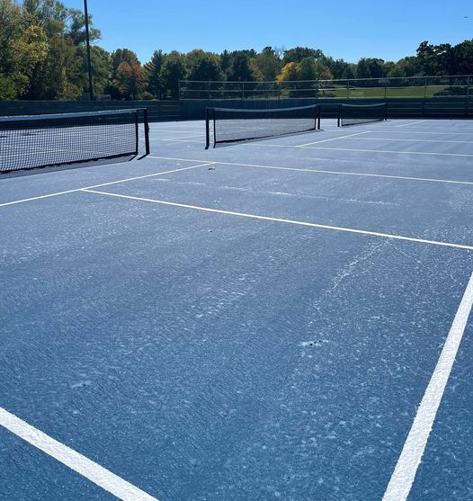 Three pickleball courts with nets, blue surfacing, and white lines with rink boards in far back.