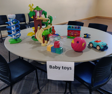 Assorted baby toys, ball, ABC sorting toy, blocks, on tabletop labeled "Baby toys" sign