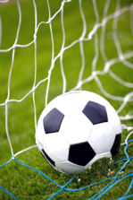 Black and white soccer ball on artificial turf field slamming against soccer net.