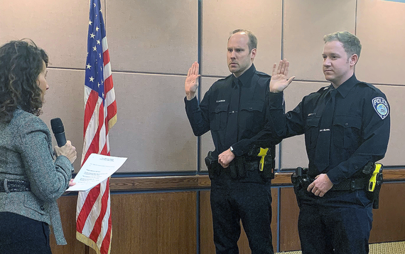 Two officers in MHPD uniforms raising their right hands taking the oath of office from Mayor Levine in Council Chambers, American Flag in background.