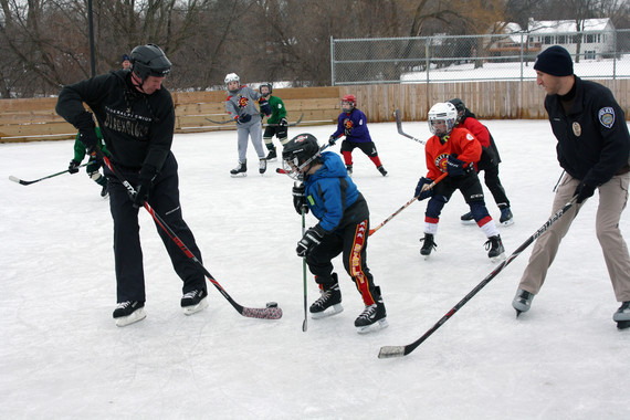 Police officers playing hockey with youth on outdoor ice rink.
