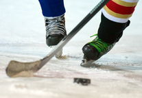 close up of hockey players' skates on ice with puck and hockey stick in motion