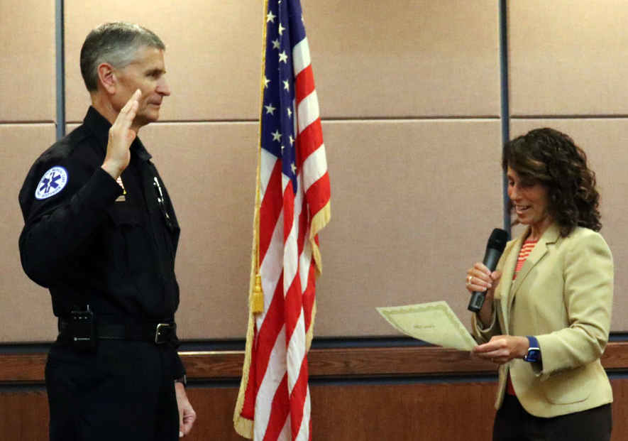 Firefighter Dan Johnson raising his right hand being sworn in as Captain by Mayor Levine in the Council Chambers, American flag in background.