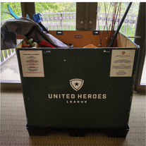 Large collection box with United Heroes League printed on front, filled with skis, fishing rods, and other sports equipment.