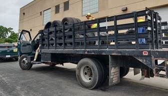 Open trailer truck with two people in safety yellow vests loading black car tires.