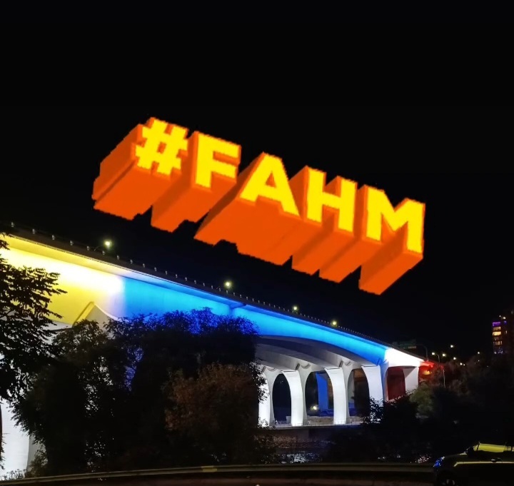 A bridge lit up in blue, yellow, and white, with #FAHM superimposed in the sky. For Filipino American History Month.