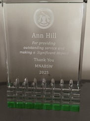 A glass award plaque featuring a dedication to Ann Hill.