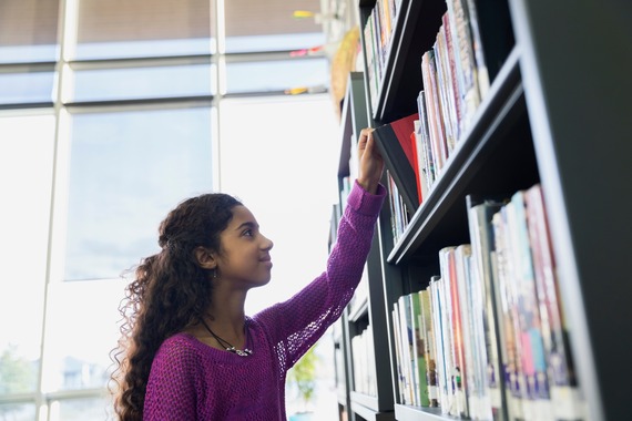 A girl looking through books on a shelf in a library