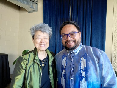 An older Asian American woman smiles next to a Filipino American man wearing traditional attire.