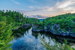 river with pine trees and rocks on both sides, cloudy sky