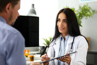 Smiling GP offering visitor sign document clipped to pad for marijuana