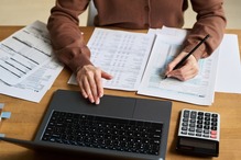 Photo of woman writing on pieces of paper next to a laptop