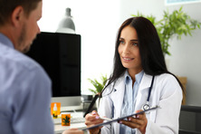 Smiling GP offering visitor sign document clipped to pad for marijuana
