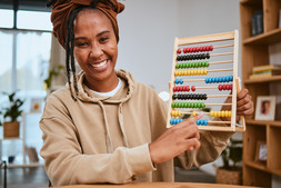 African American teacher wearing tan sweatshirt, smiling while holding an abacus counting tool