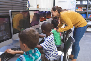 Female teacher assisting students who are working on desktop computers