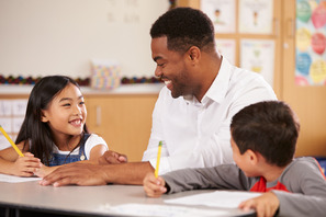 African American male teacher smiling while working with two elementary age students