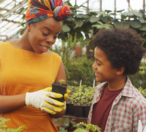 An African American female agriculture teacher showing a newly sprouted plant to an elementary-age student