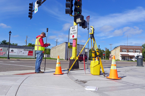 a surveyor stands at the intersection of Penn Avenue and West Broadway in Minneapolis with equipment