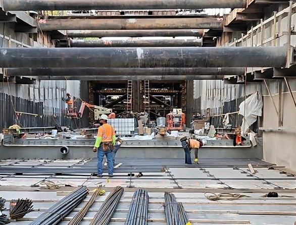 Tunnel construction including below ground excavation, installation of rebar for the tunnel floor slab, and installation of waterproofing.