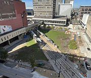 Block of open land bisected by light rail line surrounded by buildings.