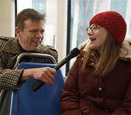 Man holding microphone and interviewing woman on train.