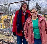 Two women standing in front of a fence.