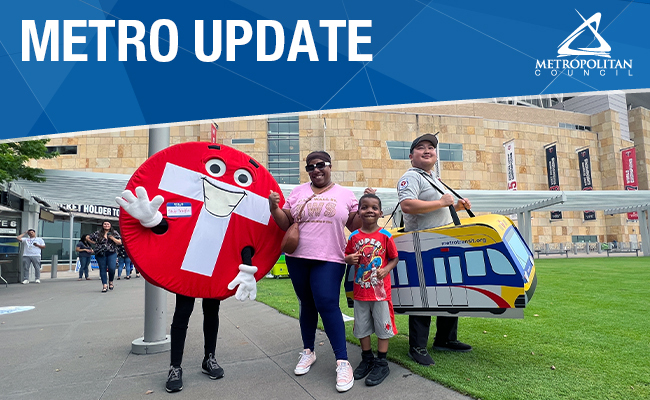 Woman and boy pose with Metro Transit's character Skip Traffic and another employee wearing a cardboard light rail car at Target Field.