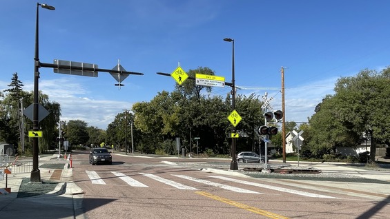 A photo of a roadway and train tracks crossing the roadway. Cars are driving on the road, which recently reopened to traffic.