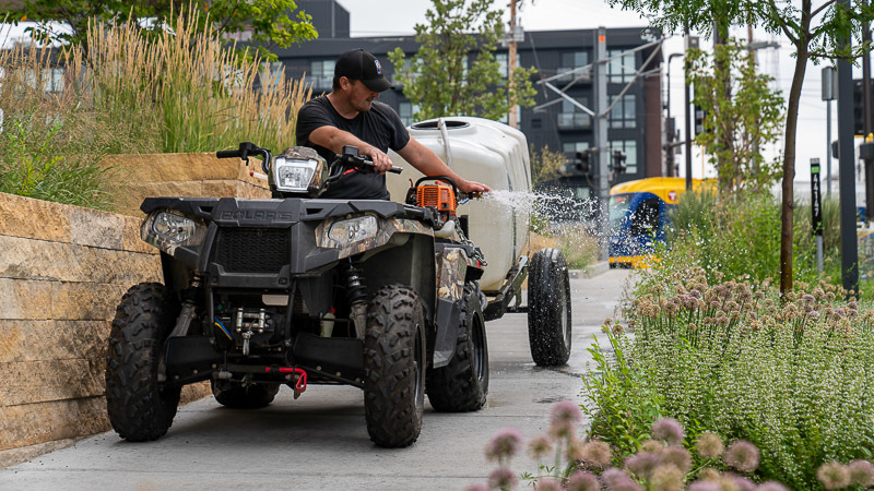 A worker watering plants from an ATV.