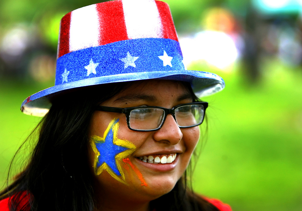 Person smiling, wearing a hat of stars and stripes with a star painted on their cheek