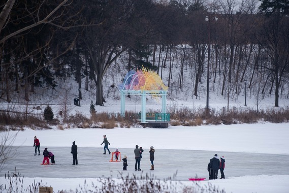 People skate on the ice rink on Powderhorn Lake with a colorful park pavilion in background