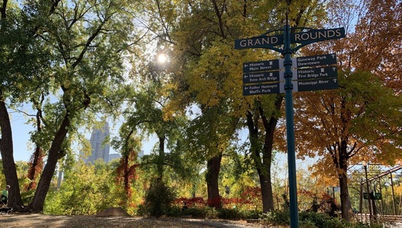 Grand Rounds Sign on Main Street in the fall with fall colors on trees and Nicollet Island Bridge