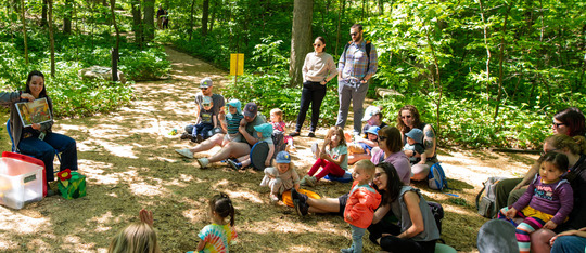 families listening to story while sitting in a clearing in the woods